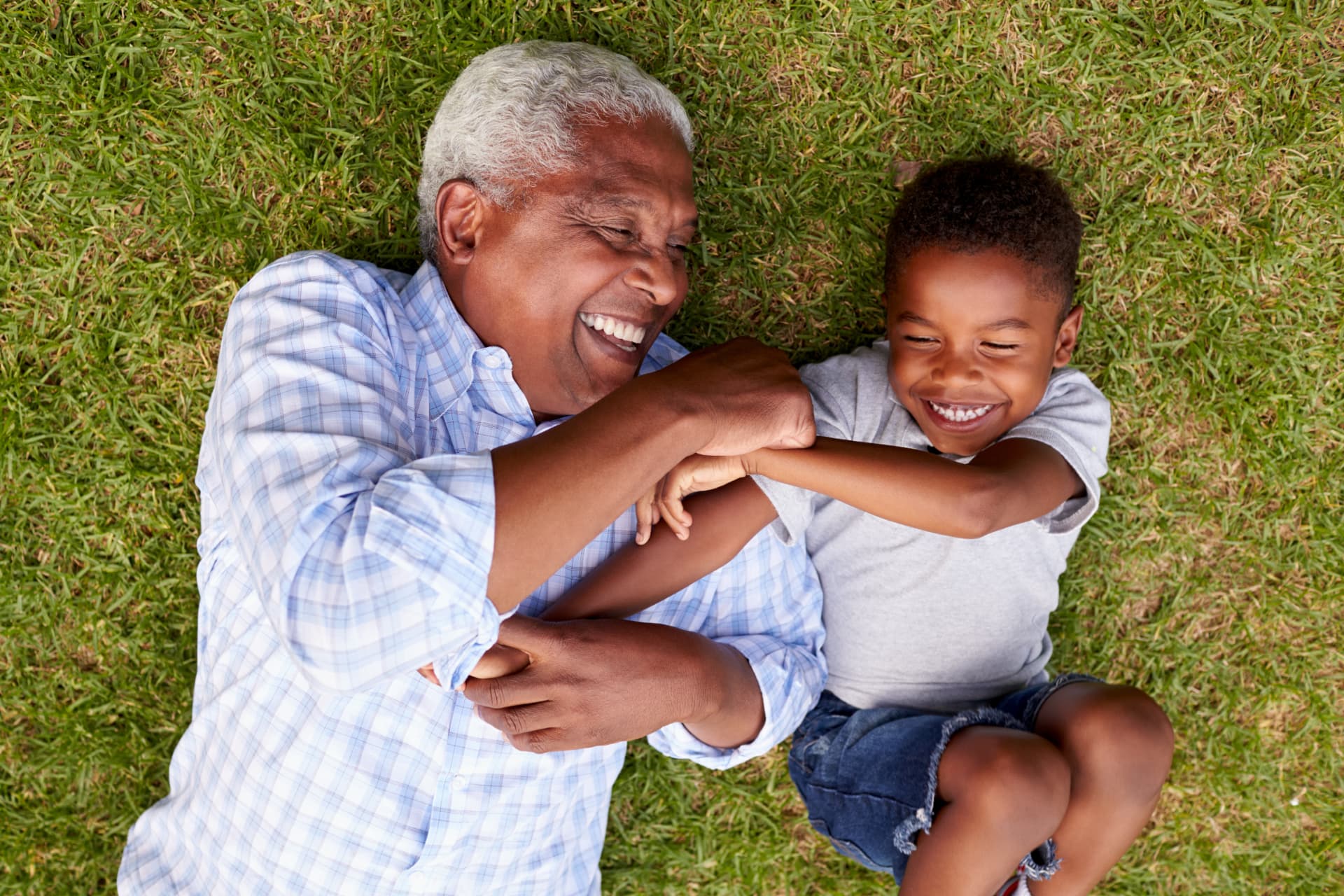 A grandfather and grandson laughing together on a green lawn