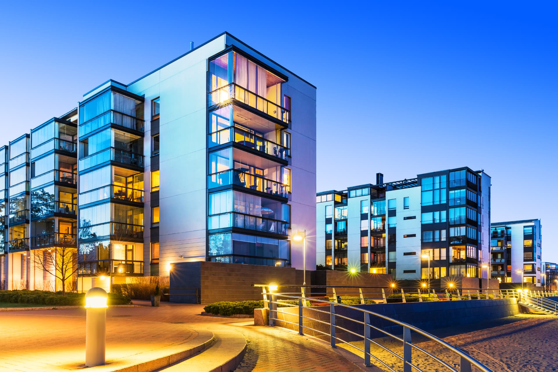 Modern residential buildings glowing at dusk along a waterfront promenade