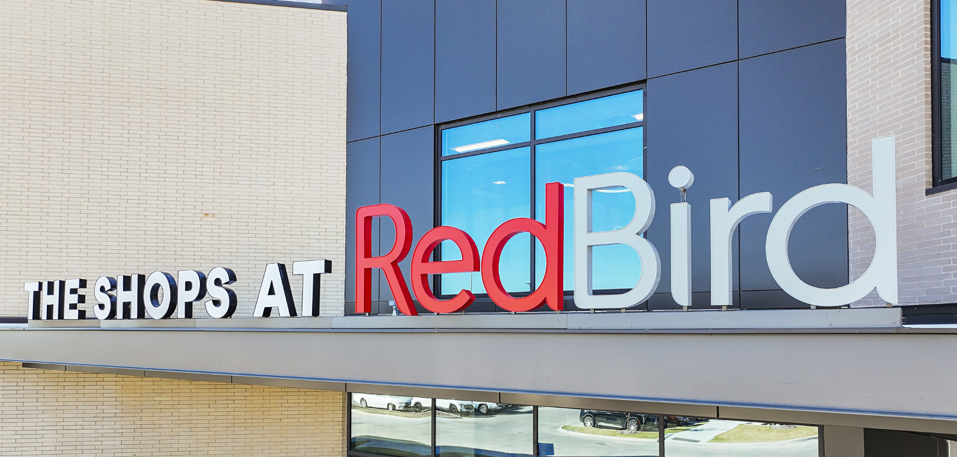 The Shops at RedBird signage mounted along the canopy ledge of the center's brick and dark-panel facade in Dallas